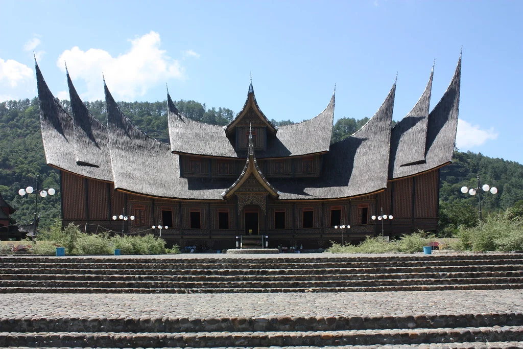 Front view of Istano Silinduang Bulan, a large wooden building with many curved gonjong roof peaks above wide stone steps