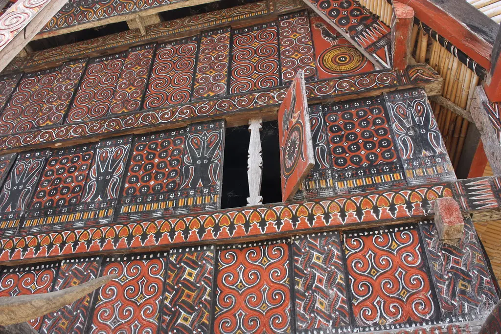 Close view of carved and painted wall panels with red, black, white and yellow spirals and geometric motifs